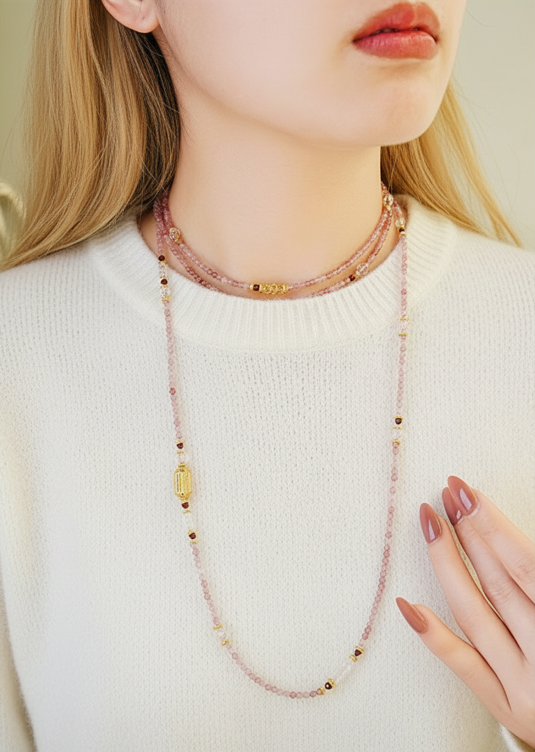 Necklace with pink beads and gold accents worn by a person on a neutral background