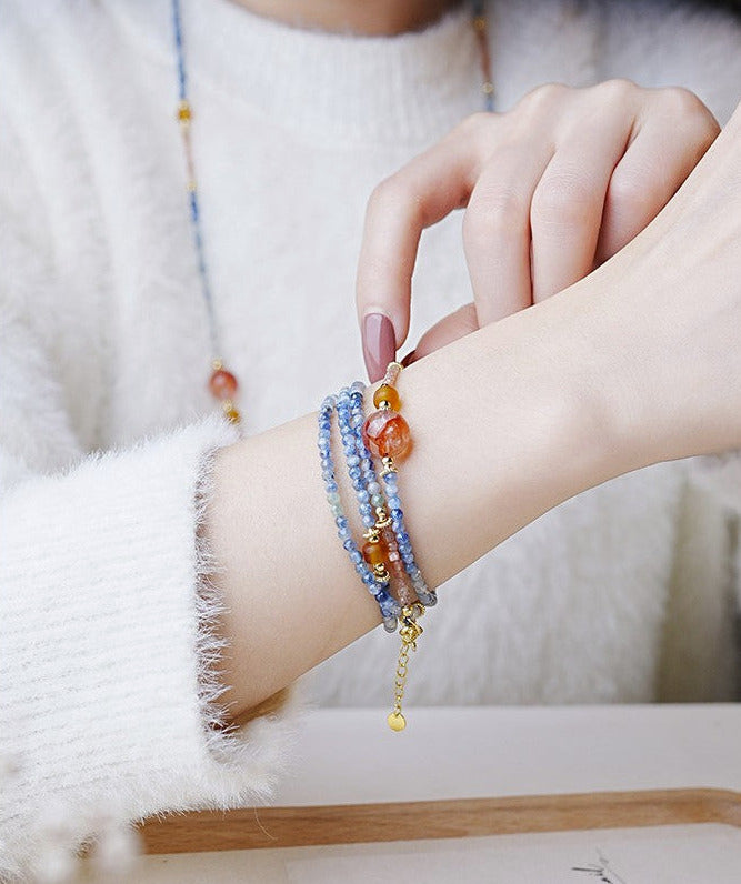 Close-up of a hand wearing multiple colorful beaded bracelets on a soft white background.