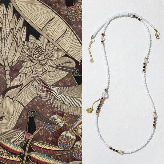 Necklace with beaded chain on a white background, next to an illustration of tropical plants and birds.