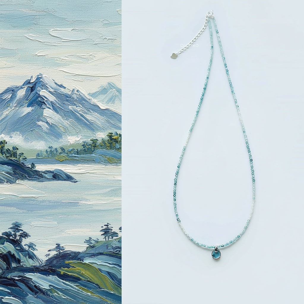 Necklace with a blue pendant next to a painting of a mountain landscape