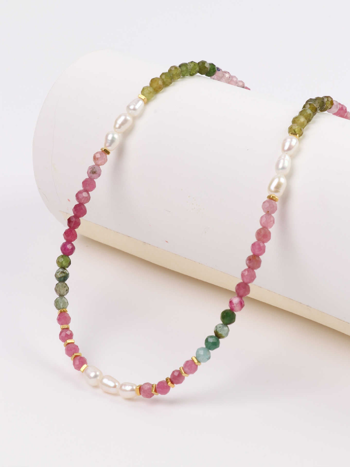 Beaded necklace with pink and green beads on a white surface