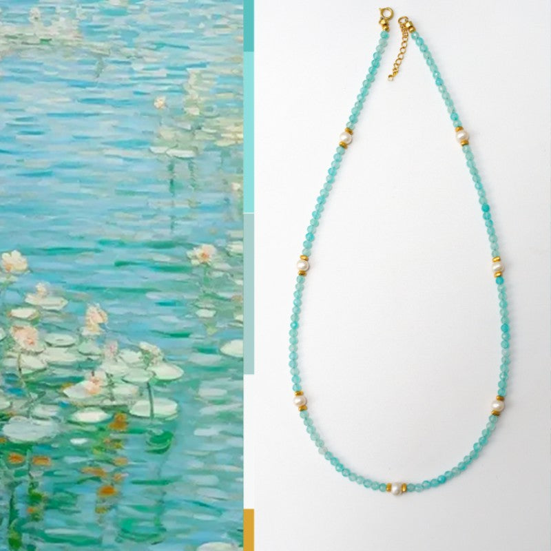 Necklace with blue beads and gold accents next to a painting of water lilies