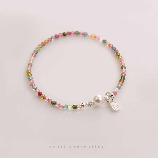 A multicolor tourmaline and pearl bracelet with a sterling silver blessing tag, displayed against a light background.