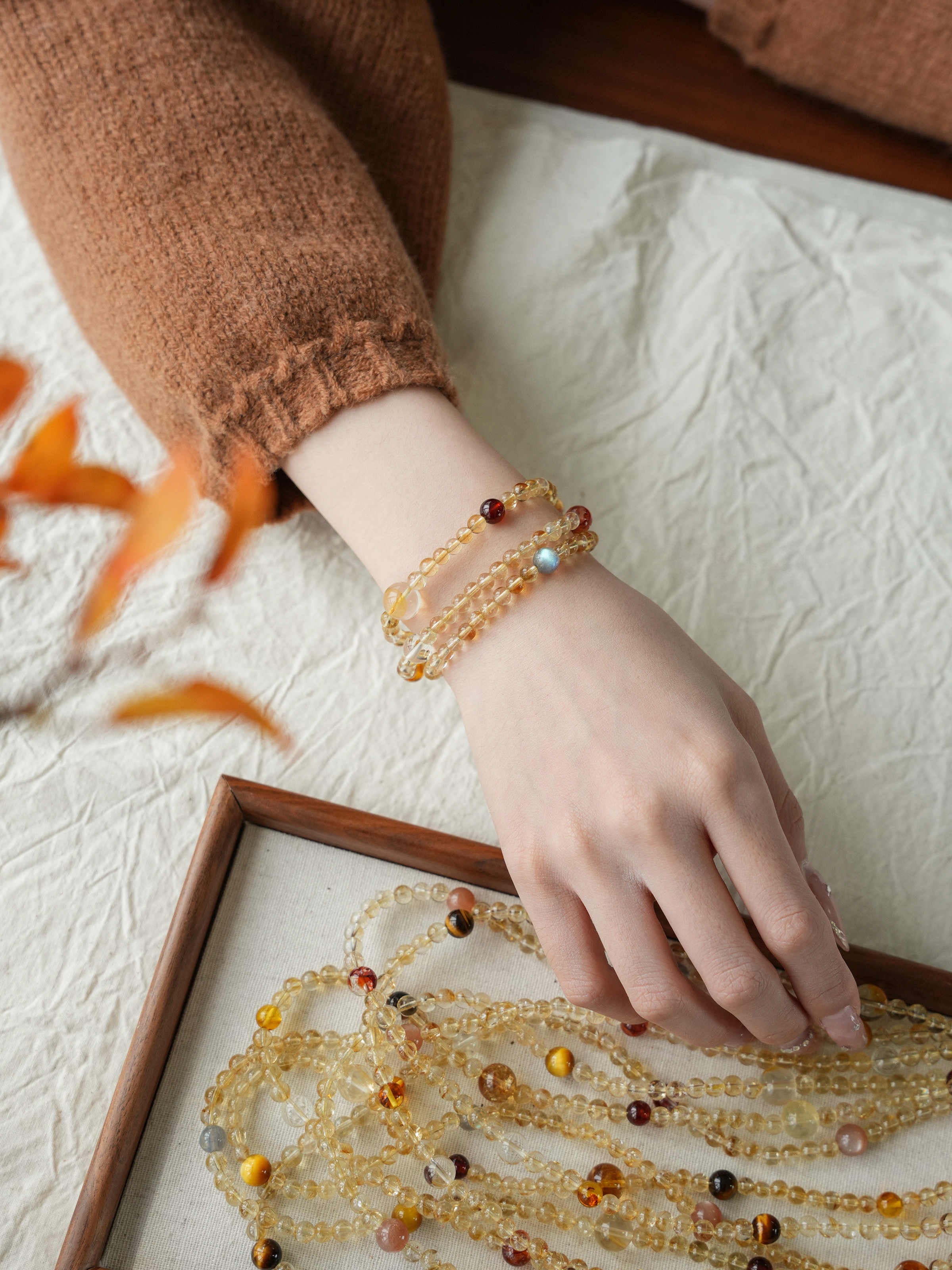 Hand wearing a beaded bracelet on a textured surface with a branch in the background