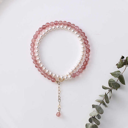 Two beaded bracelets, one pink and one white, on a white surface with a sprig of eucalyptus.