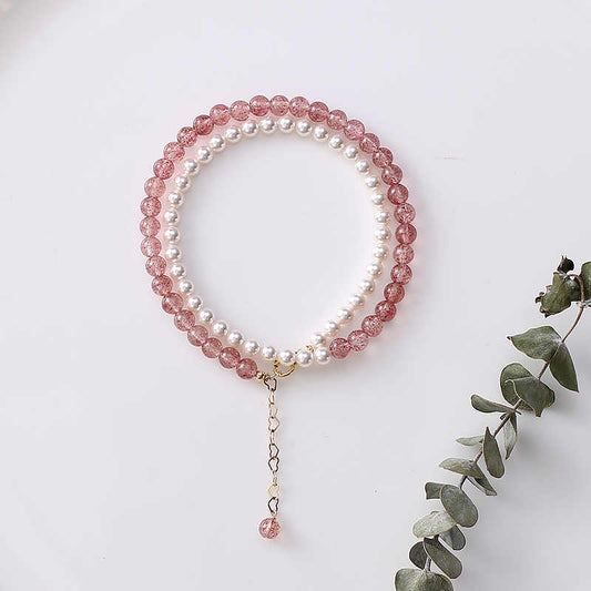 Two beaded bracelets, one pink and one white, on a white surface with a sprig of eucalyptus.