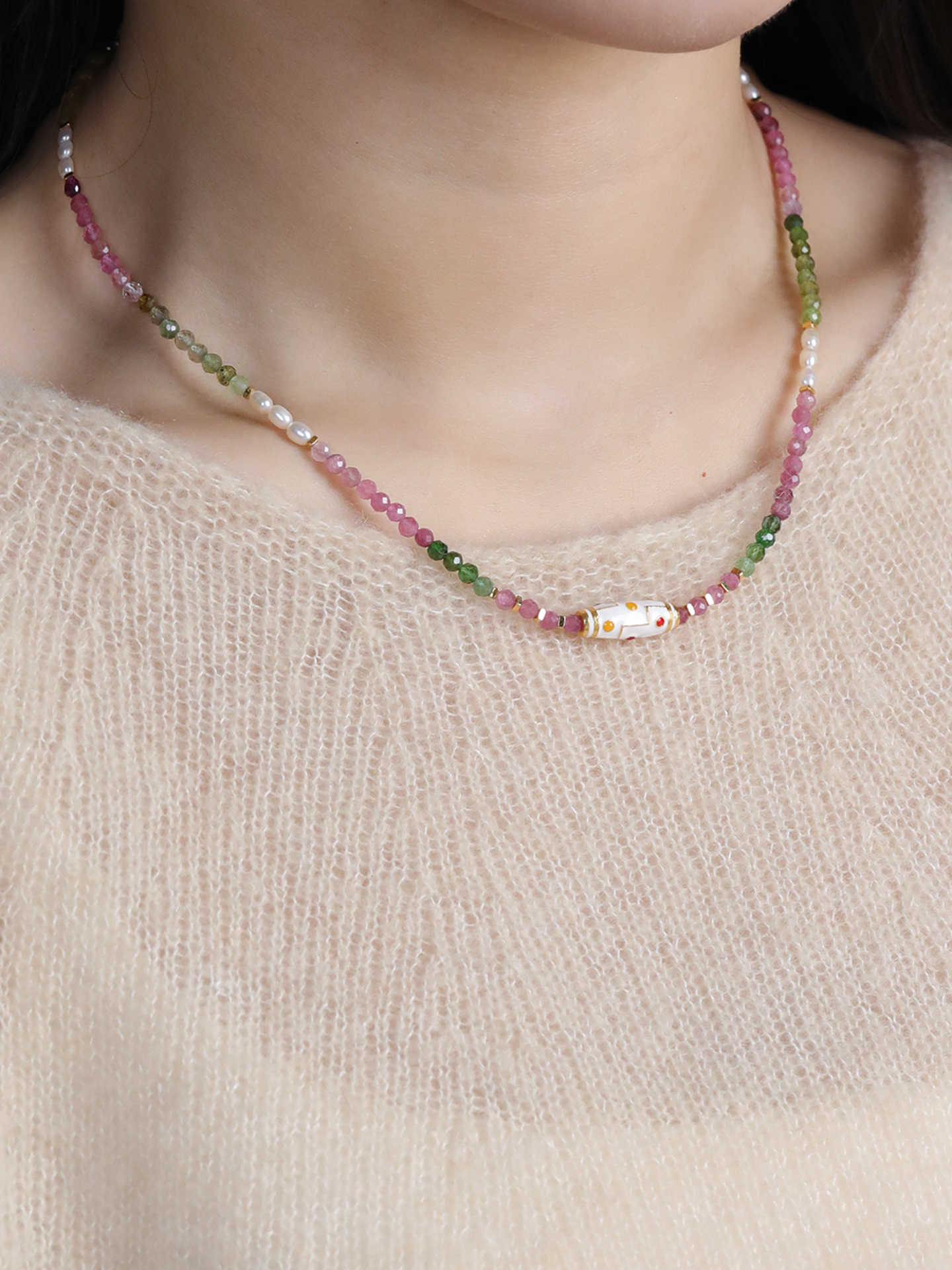 Necklace with multicolored beads worn by a person against a neutral background