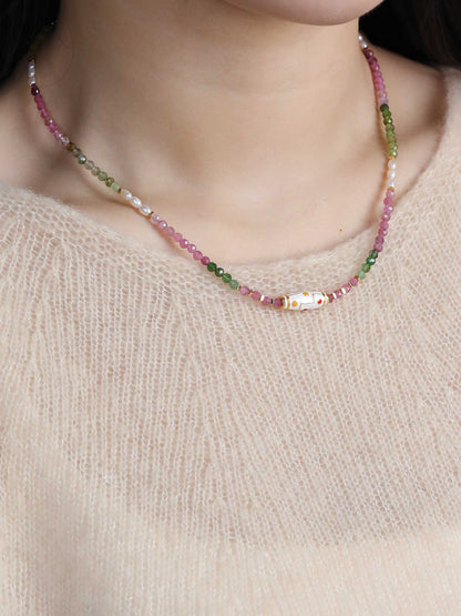 Necklace with multicolored beads worn by a person against a neutral background