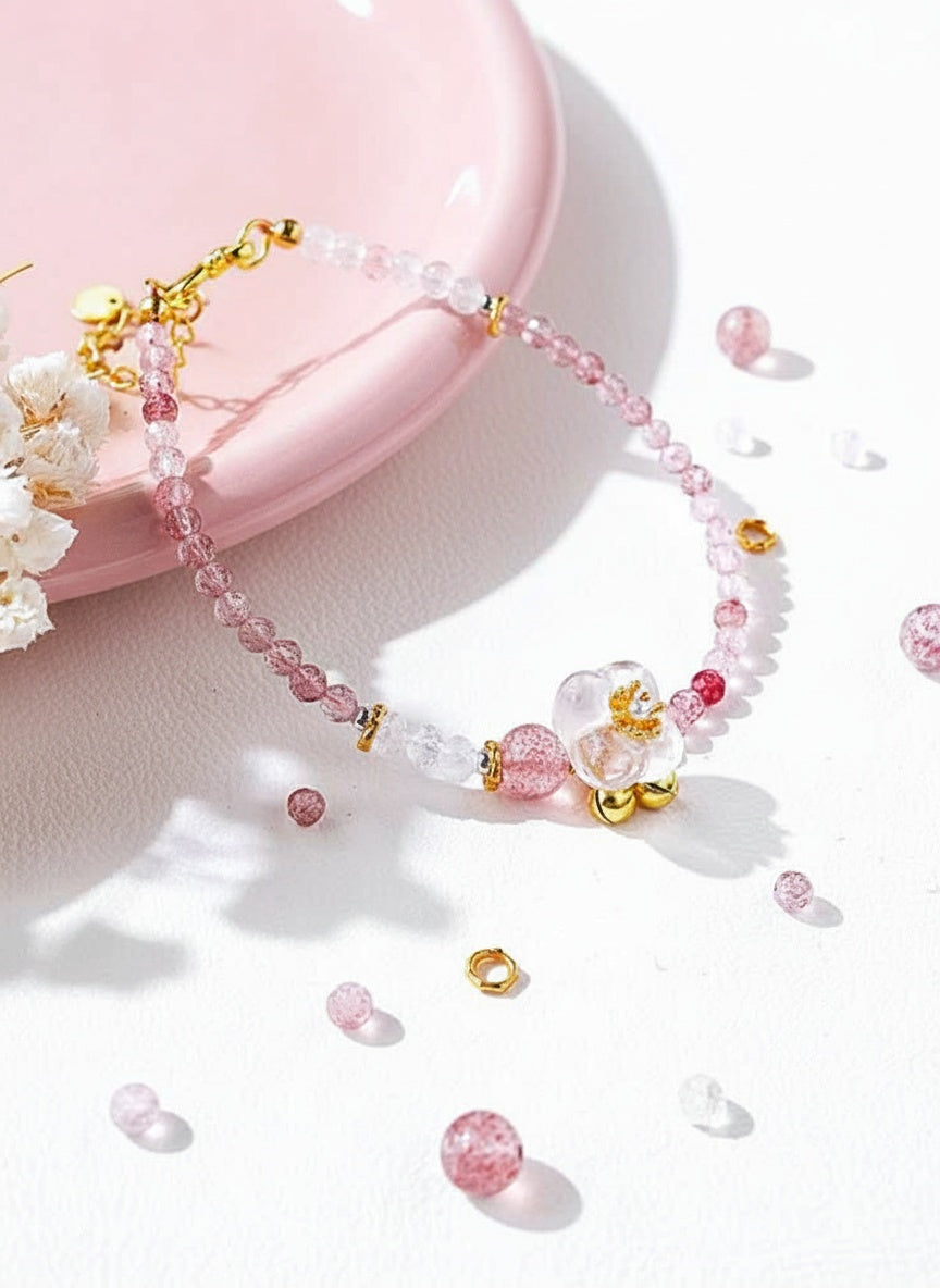 Pink beaded necklace with gold accents on a white surface with pink flowers.
