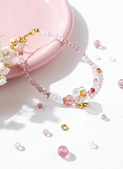 Pink beaded necklace with gold accents on a white surface with pink flowers.