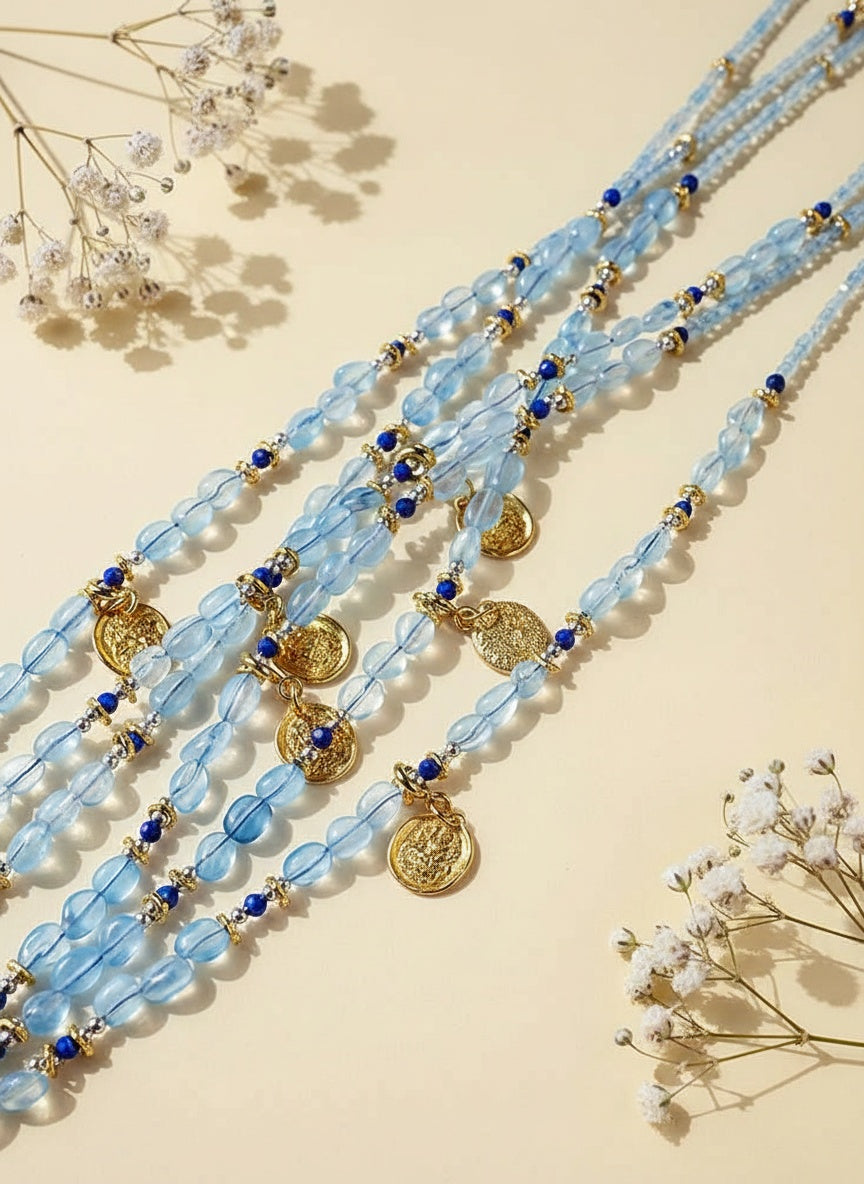 Blue beaded necklace with gold accents on a beige background with white flowers.