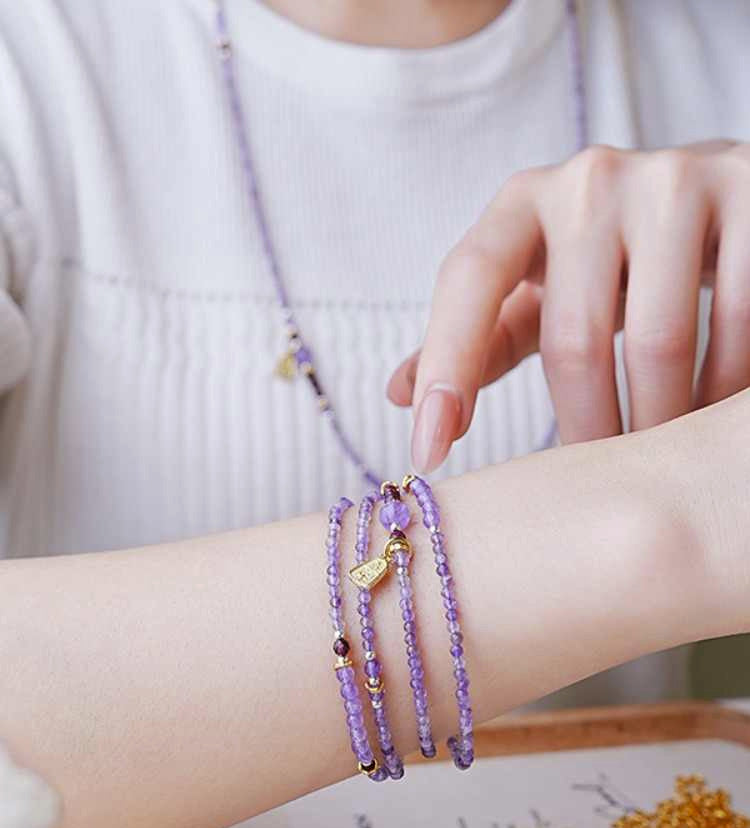 Person wearing a stack of purple beaded bracelets on their wrist with a blurred background.