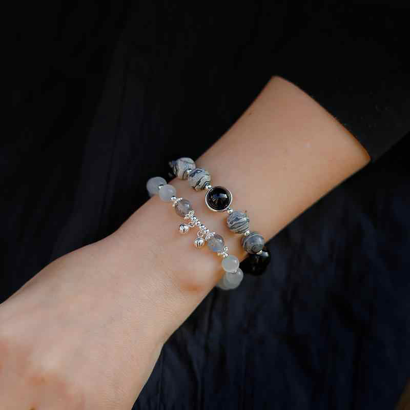 Close-up of a wrist wearing two beaded bracelets against a dark background.