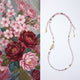 Beaded necklace with pink and gold accents on a white background, next to a floral pattern.
