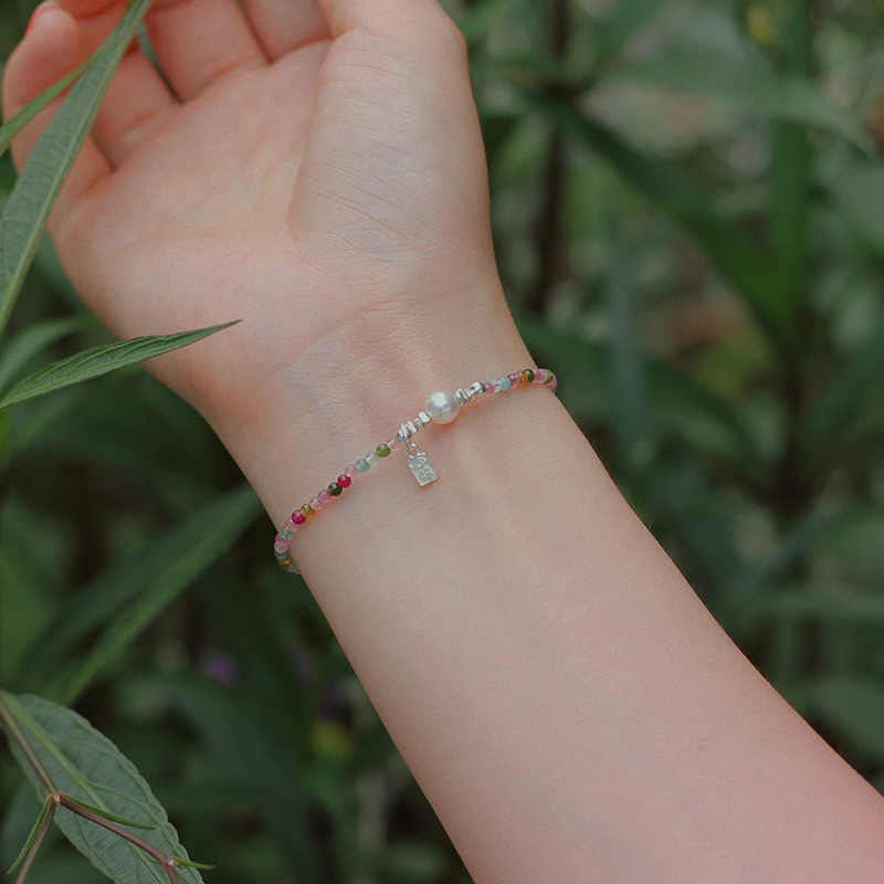 Hand wearing a colorful beaded bracelet with a natural background