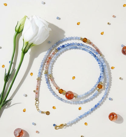 Multicolored beaded necklace on a light surface with flowers and small decorative items.