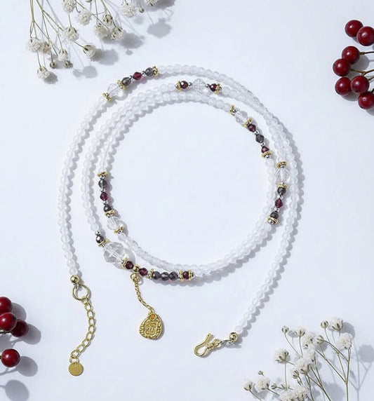 White beaded necklace with gold and red accents on a white background with dried flowers and berries.