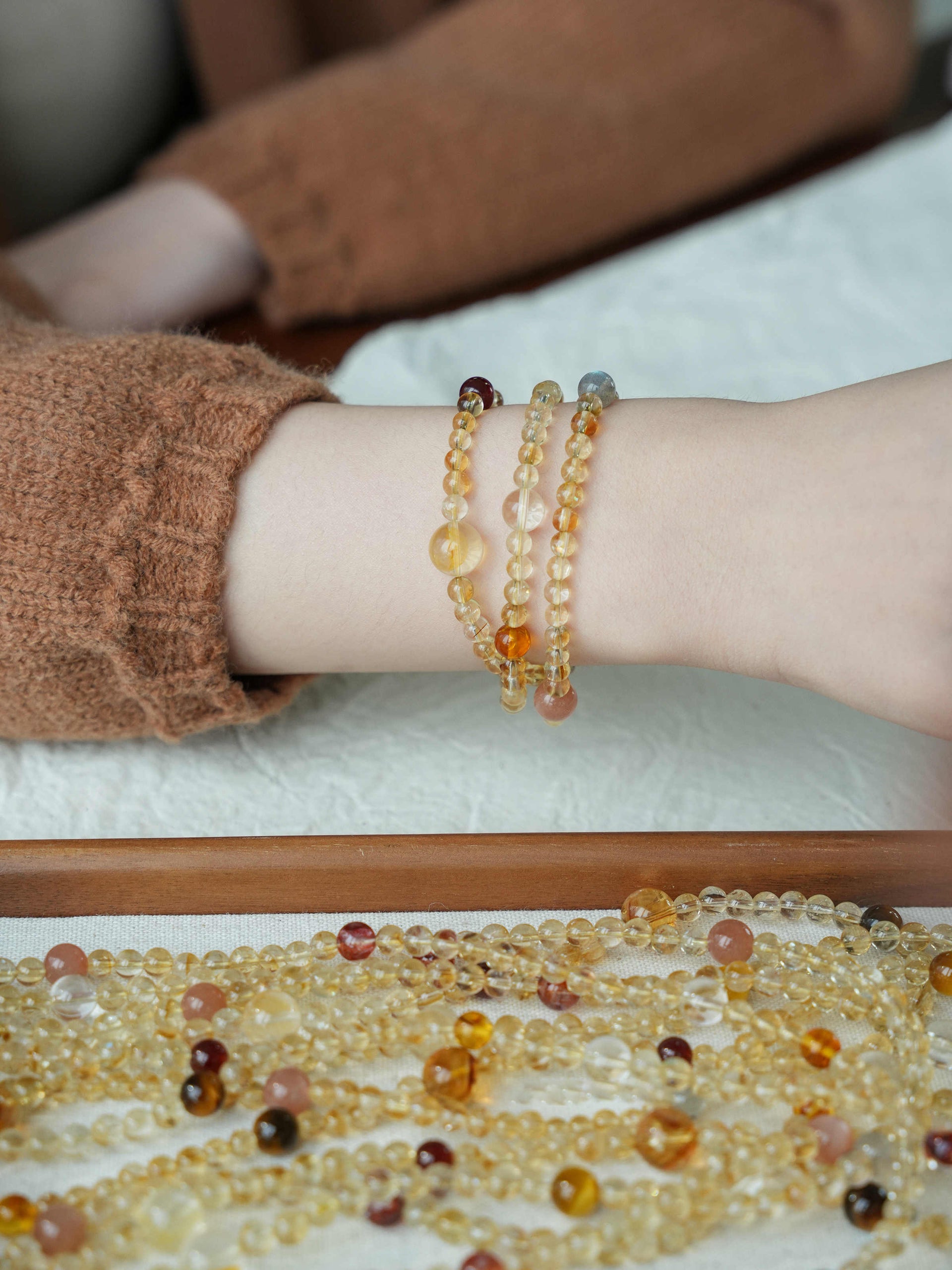 Close-up of a wrist wearing two beaded bracelets with a necklace of similar beads on a white surface.