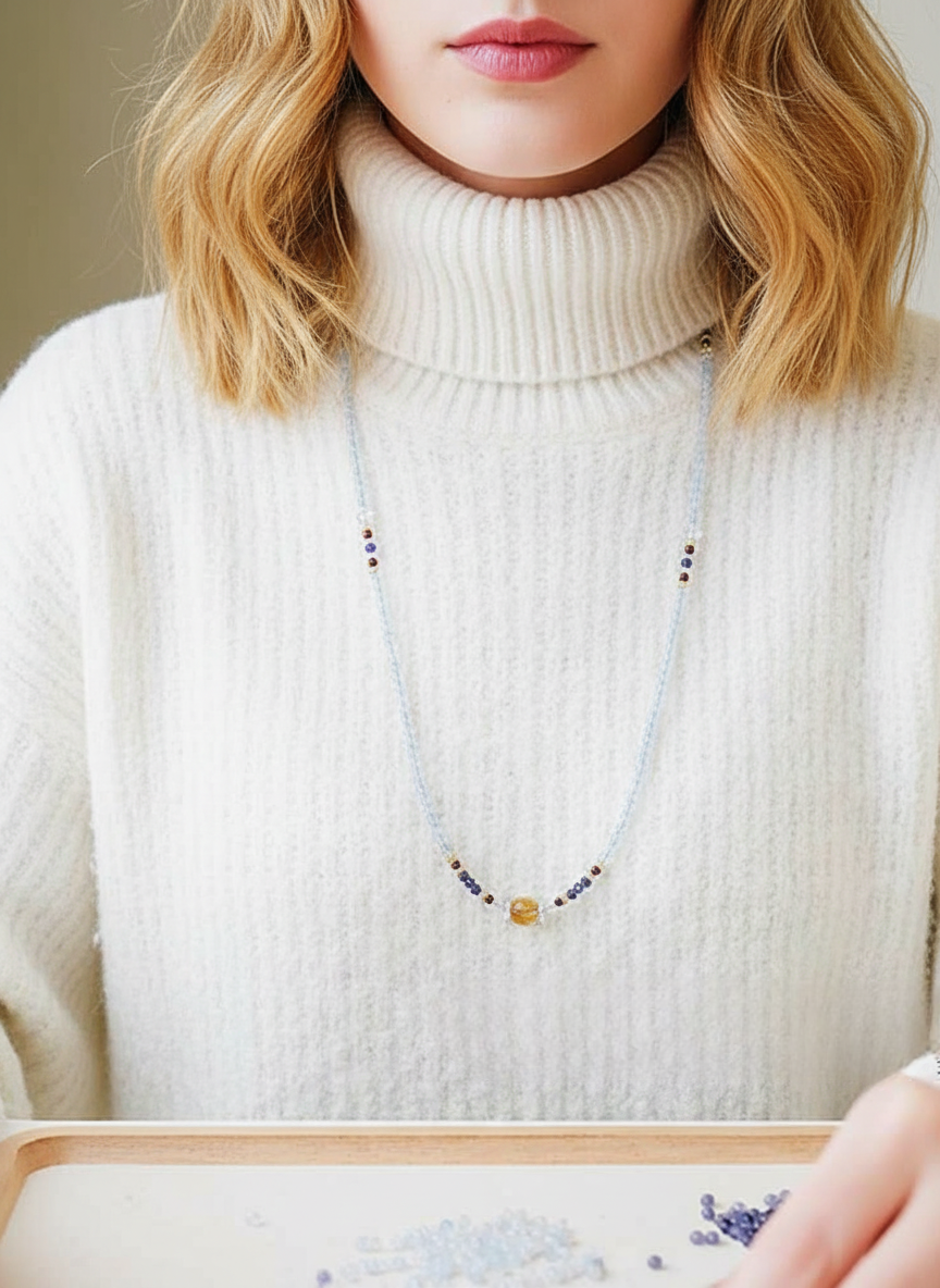 Person wearing a white turtleneck sweater with a beaded necklace
