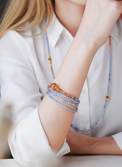 Person wearing a white shirt with colorful beaded bracelets on a plain background