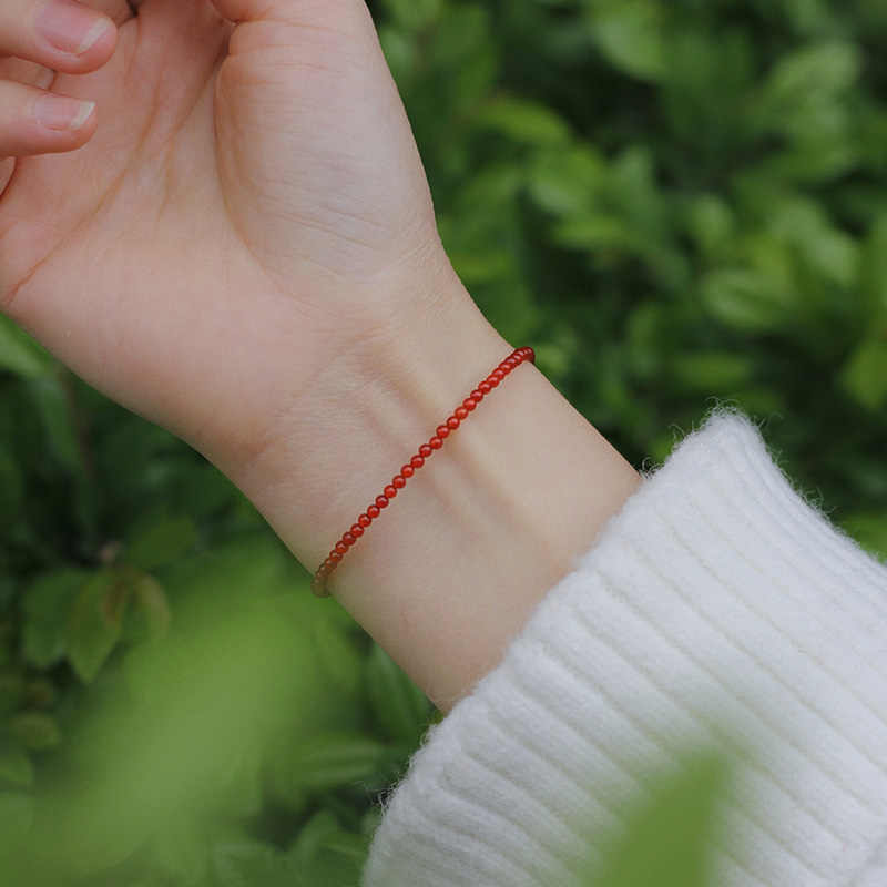 Red beaded bracelet on wrist with green background
