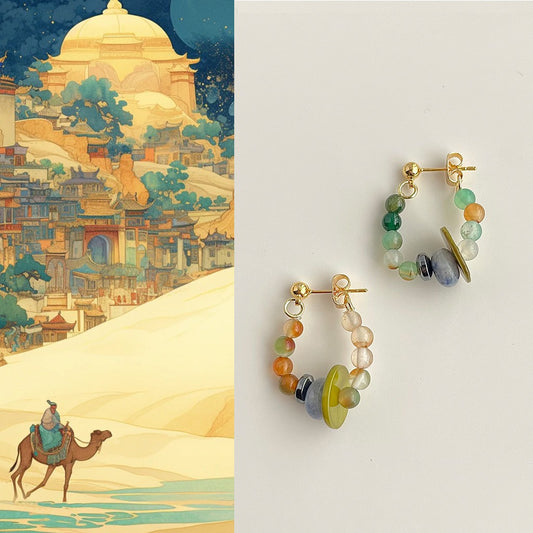 Colorful hoop earrings with gemstones on a white background, next to an illustrated scene of a camel caravan in a desert landscape.