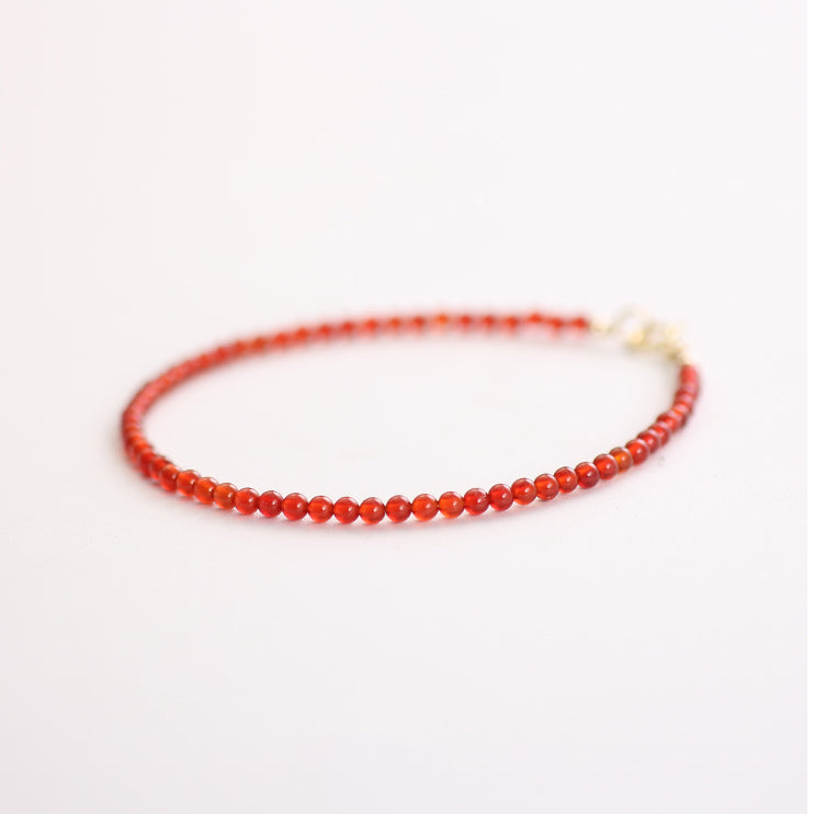 Thin red beaded bracelet on a white background
