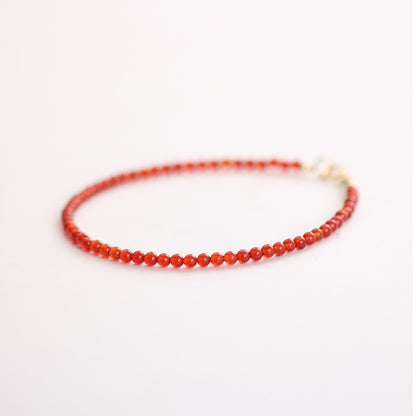 Thin red beaded bracelet on a white background