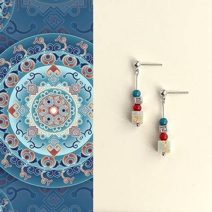 Decorative earrings with colorful beads on a beige background, next to a patterned blue and orange plate.