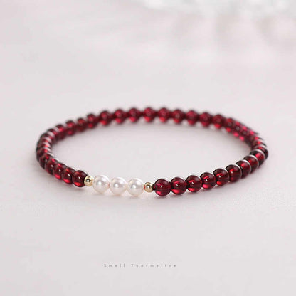 A bracelet with deep red natural garnet beads and white freshwater pearls, with gold-toned spacers and a comfortable elastic fit.