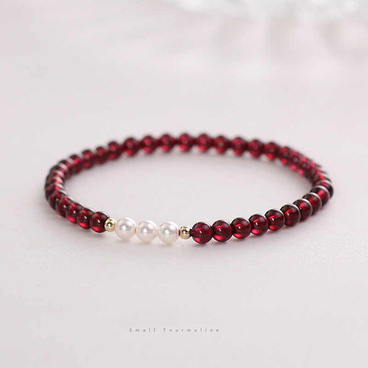 A bracelet with deep red natural garnet beads and white freshwater pearls, with gold-toned spacers and a comfortable elastic fit.