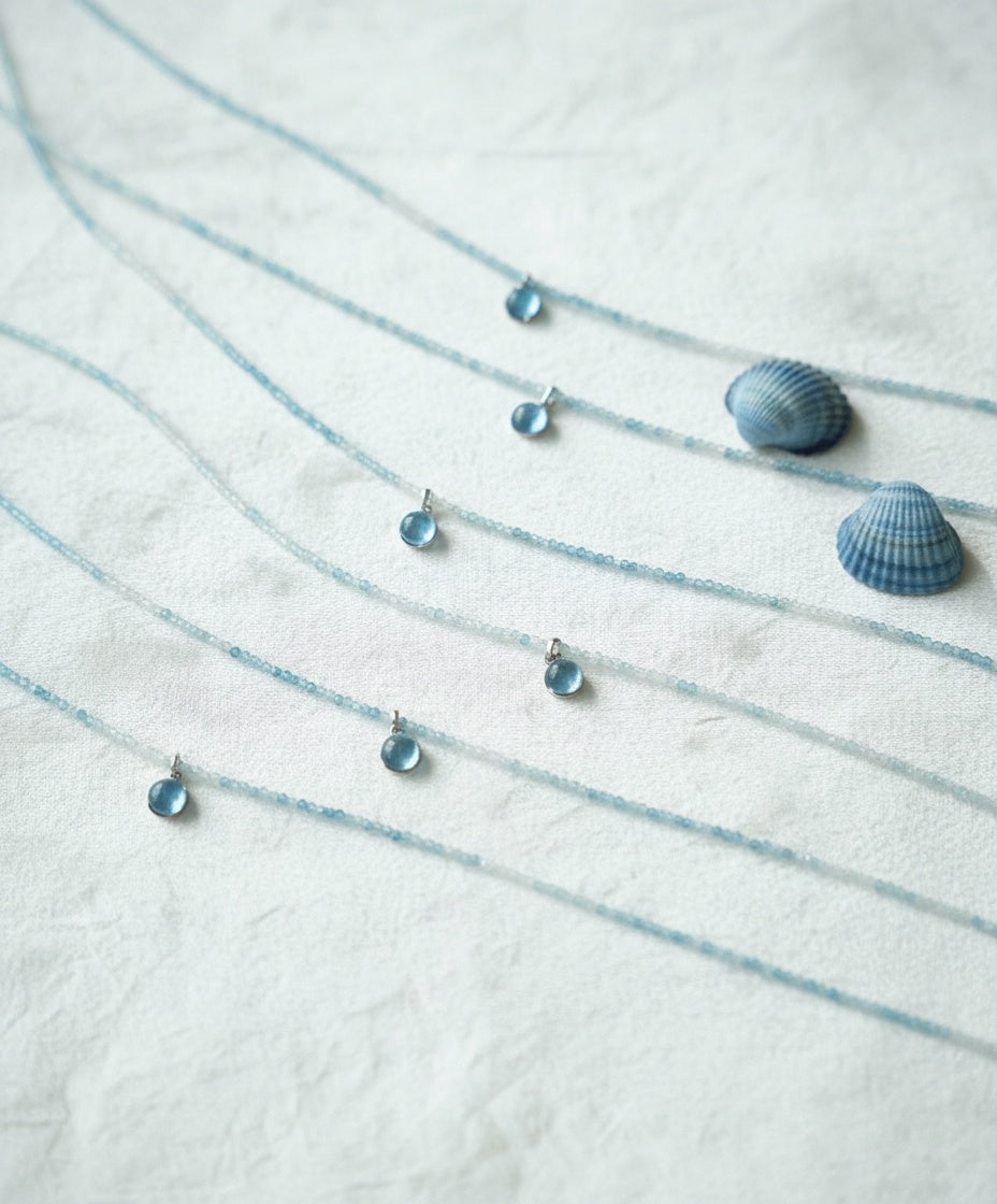Blue necklace with matching pendants and seashells on a white fabric background