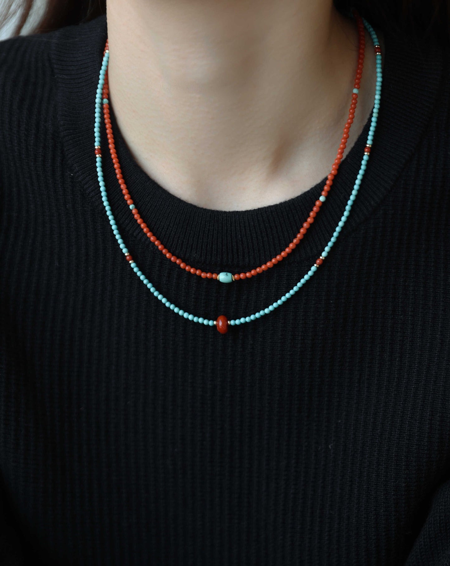Two beaded necklaces, one turquoise and one orange, on a black sweater.