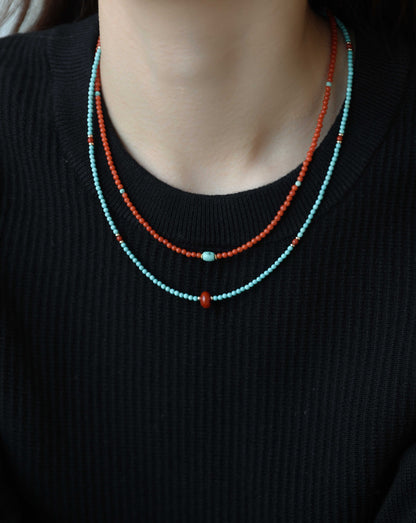 Two beaded necklaces, one turquoise and one orange, on a black sweater.