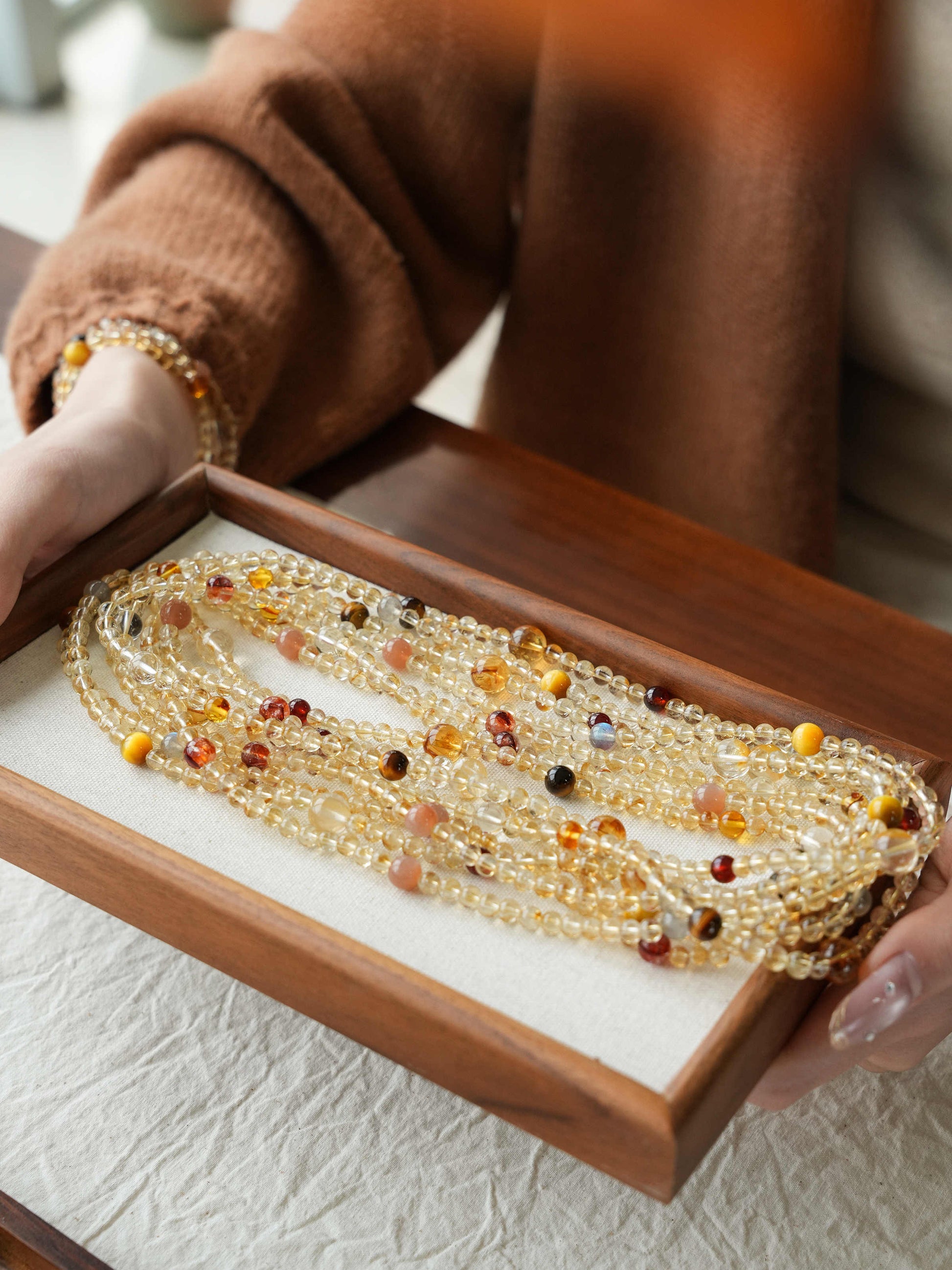 Beaded necklace in a wooden box held by a person wearing a brown coat.
