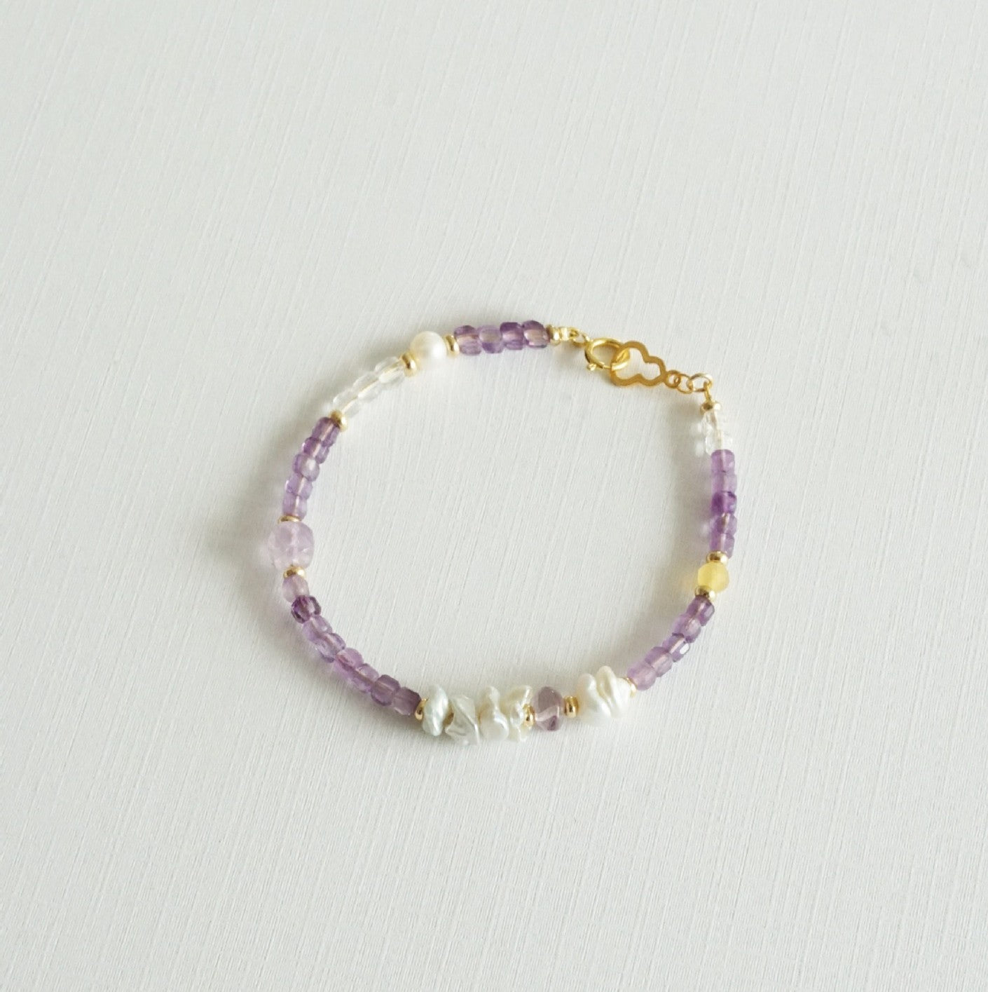 Beaded bracelet with purple and gold accents on a light gray background