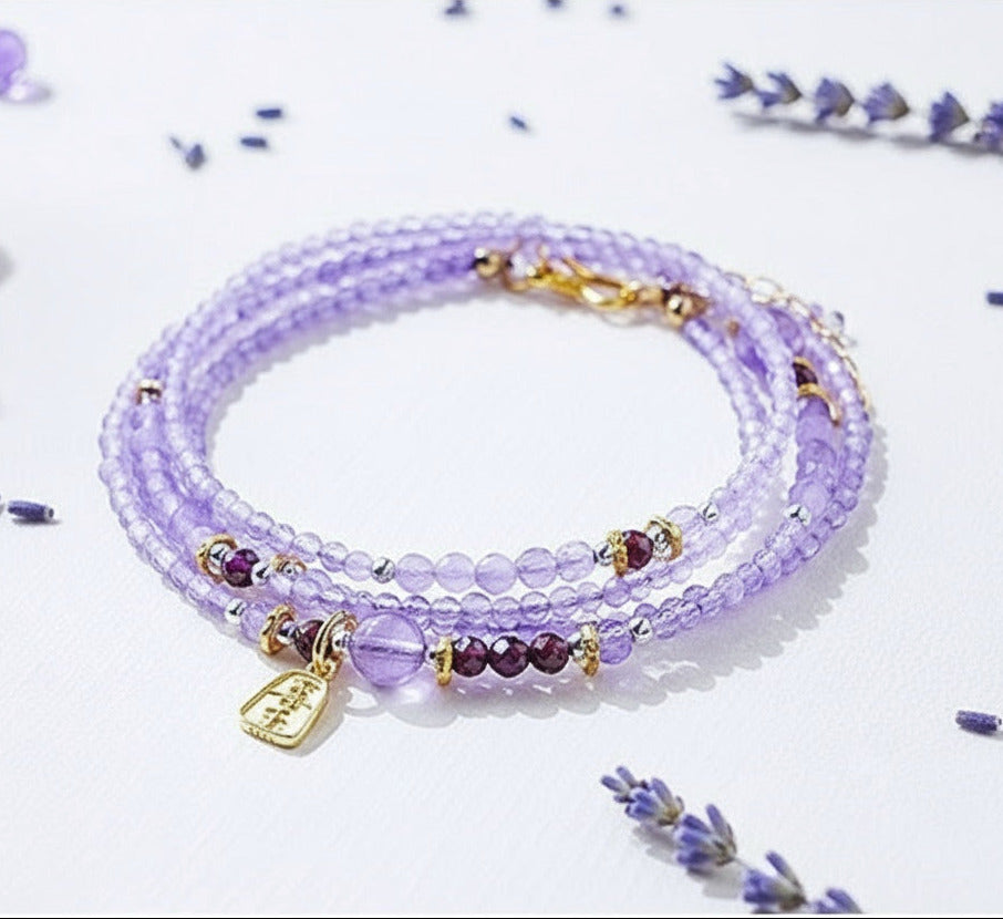 Purple beaded bracelet with gold accents on a light purple background with lavender flowers.