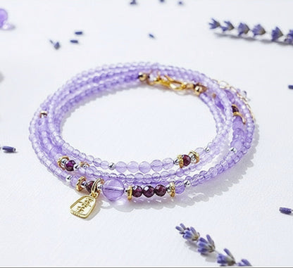 Purple beaded bracelet with gold accents on a light purple background with lavender flowers.