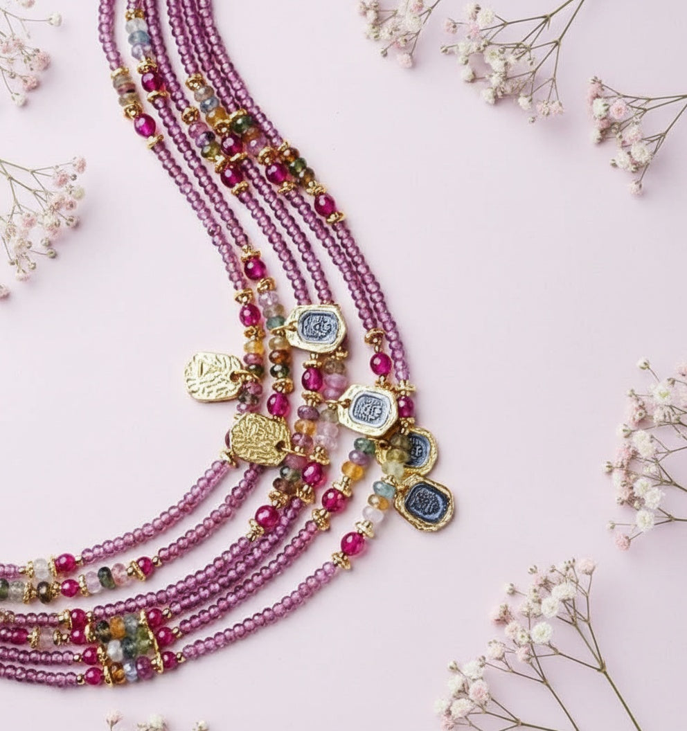 Multistrand beaded necklace with colorful beads and gold accents on a light pink background with dried flowers.