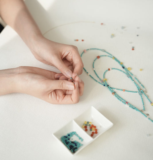 Hands working with beads on a white surface