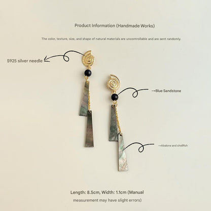 Pair of earrings with gold accents and blue sandstone elements on a light beige background