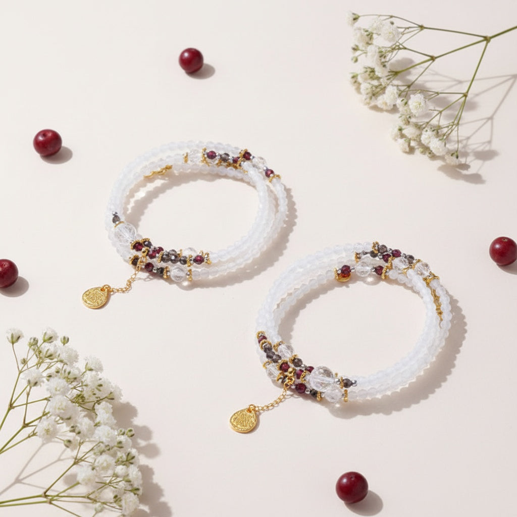 Two white beaded bracelets with gold and red beads on a light pink background with red berries and white flowers.