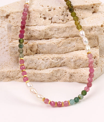 Beaded necklace with pink, green, and white beads on a stone background