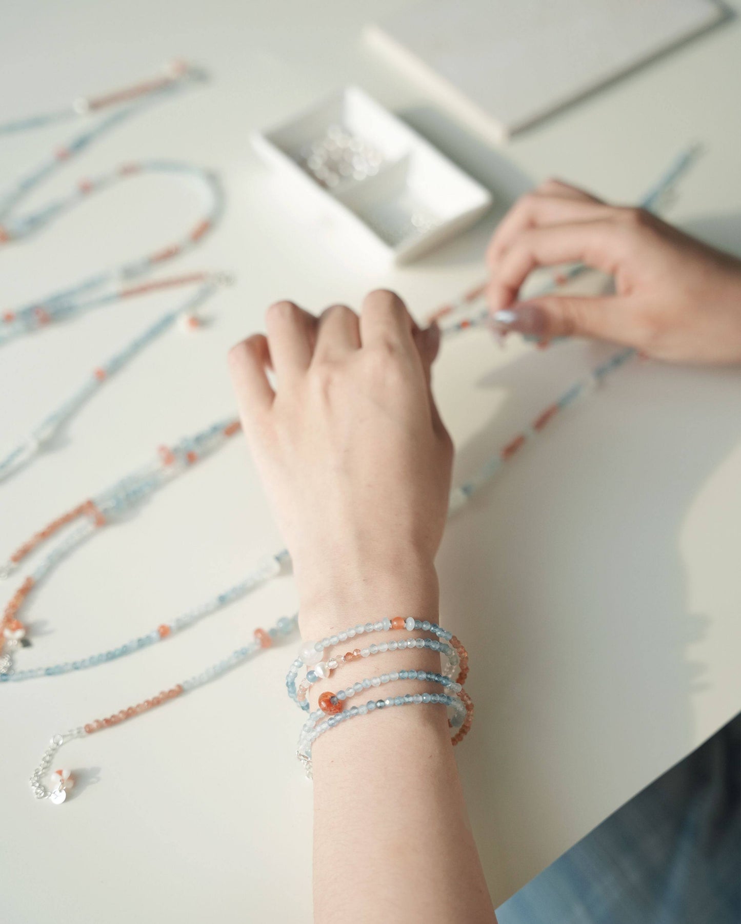 Person wearing multiple bracelets on a light surface with additional bracelets scattered around.