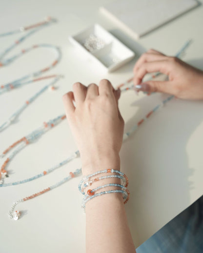 Person wearing multiple bracelets on a light surface with additional bracelets scattered around.
