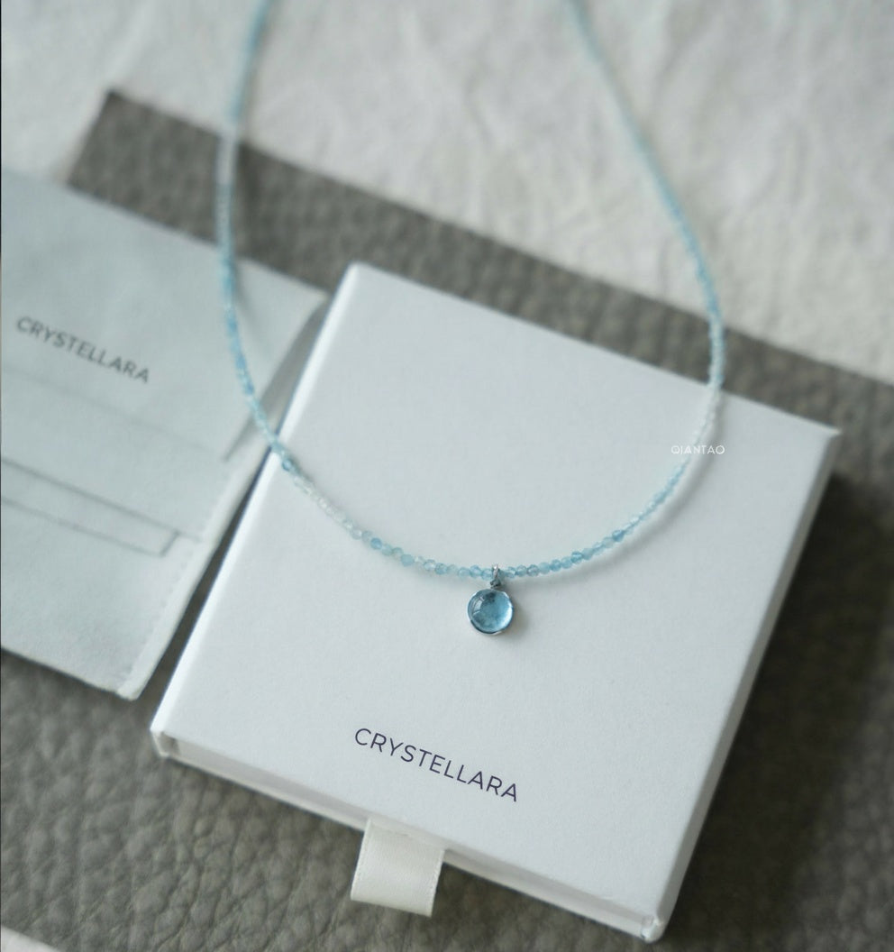 Blue necklace with a pendant on a white box labeled 'CRYSTELLARA'.