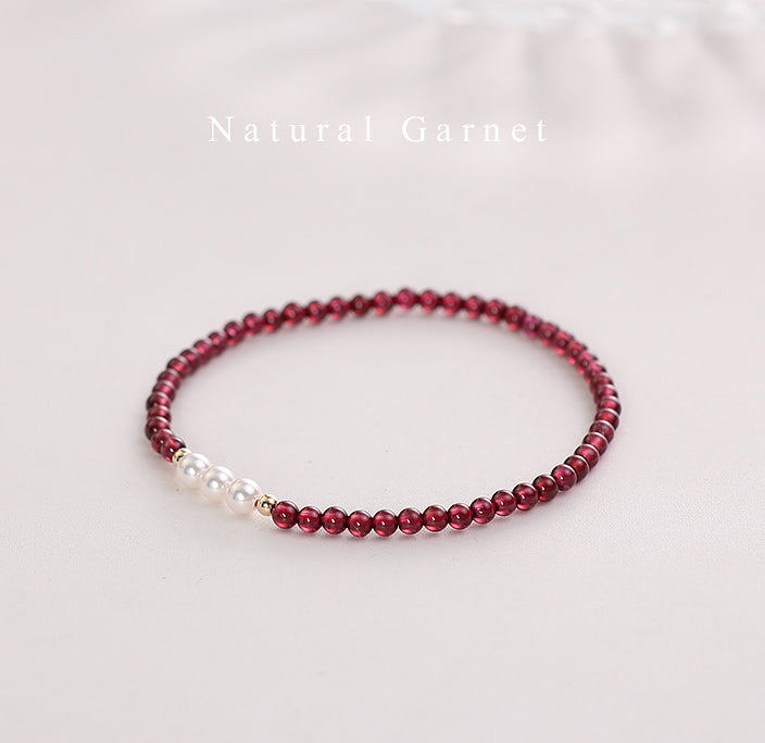 Beaded bracelet with red garnet beads and a pearl on a light background.