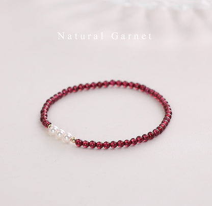 Beaded bracelet with red garnet beads and a pearl on a light background.