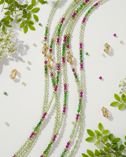 Green and pink beaded necklaces with gold accents on a white background with green leaves.