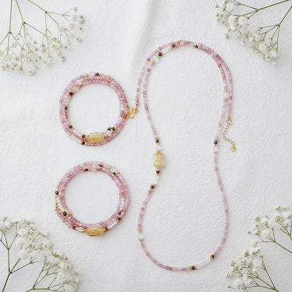 Pink beaded necklace and bracelet set on a light background with small white flowers.